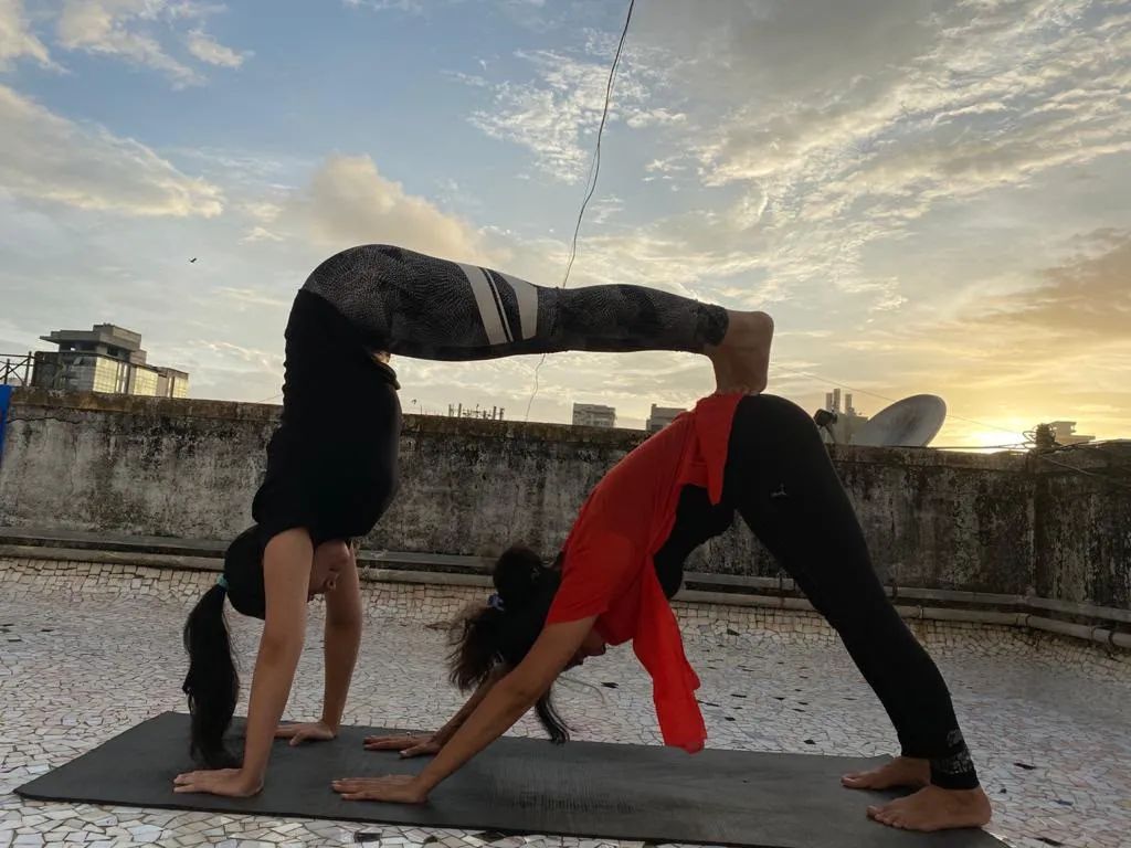 Partner downward dog on a rooftop mat under an evening sky